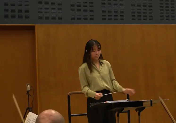 A woman is standing in front of a music stand, likely preparing to perform